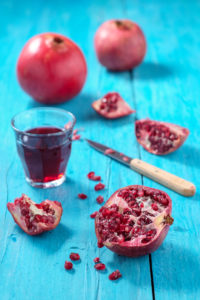 Ganze und aufgeschnittene Granatäpfel und Glas mit Granatapfelsaft auf türkisem Holztisch Ganze und aufgeschnittene Granatäpfel und Glas mit Granatapfelsaft auf türkisem Holztisch